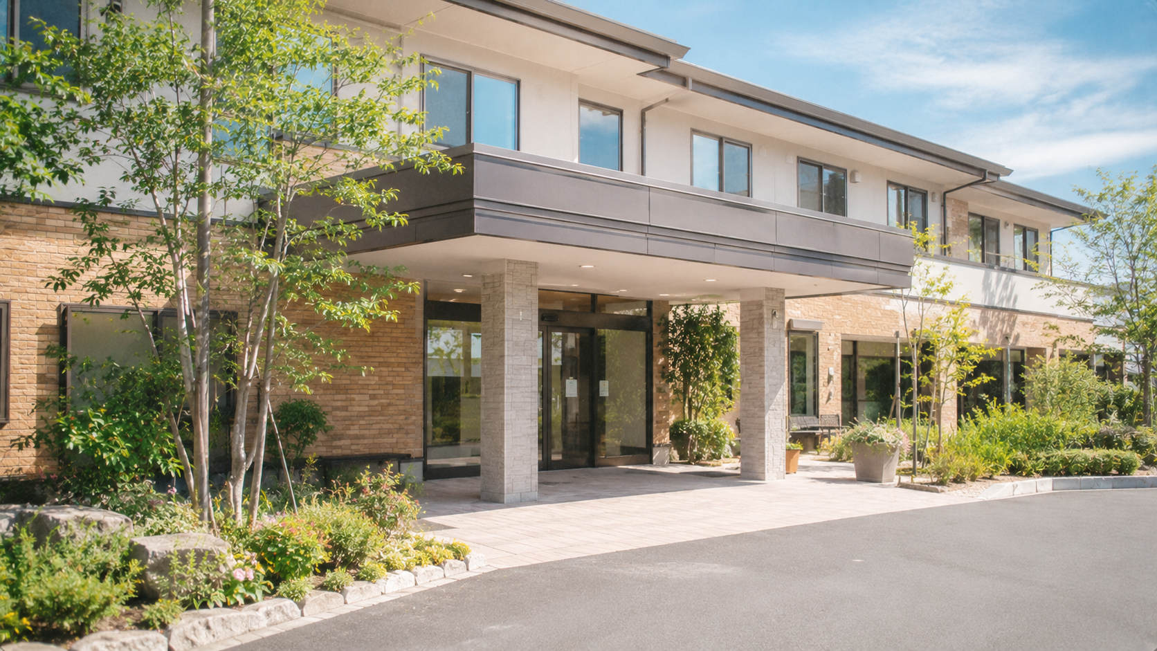 日差しの中に佇む介護施設のエントランス。緑と石畳が広がる住宅型有料老人ホームの外観